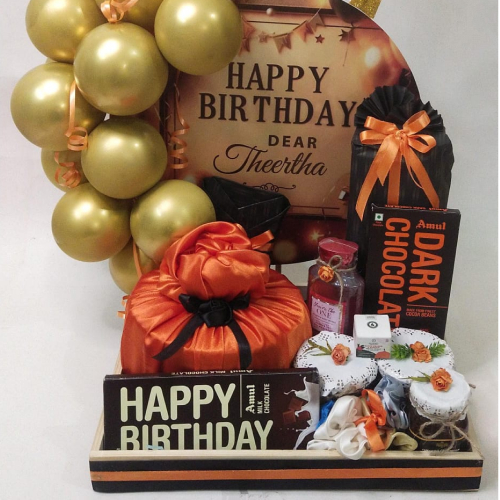 Happy Birthday hamper with Assorted chocolates, gold balloons and wrapped gifts in orange cloth